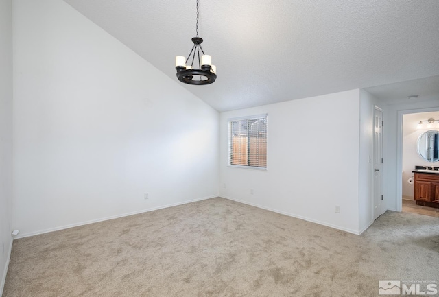 carpeted spare room featuring vaulted ceiling, a textured ceiling, and an inviting chandelier