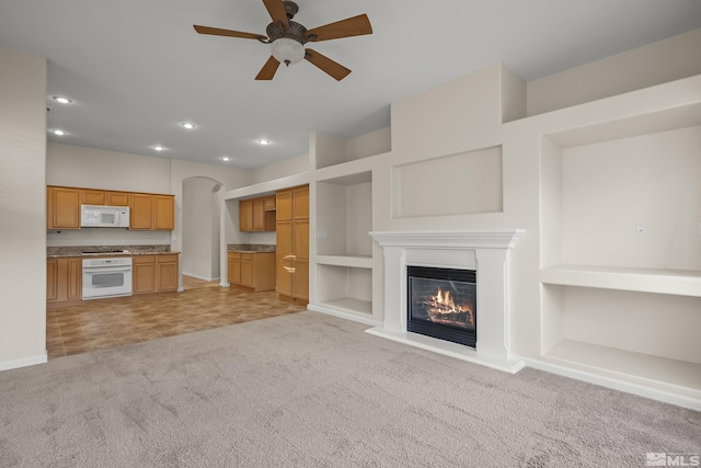 unfurnished living room featuring light carpet, built in features, and ceiling fan