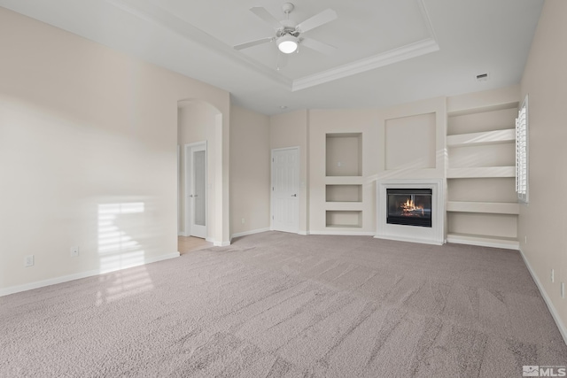 unfurnished living room featuring ceiling fan, built in features, a tray ceiling, carpet, and ornamental molding