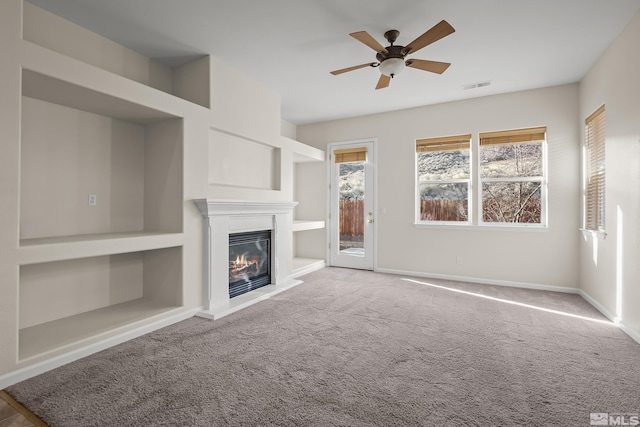 unfurnished living room with built in shelves, ceiling fan, and carpet floors