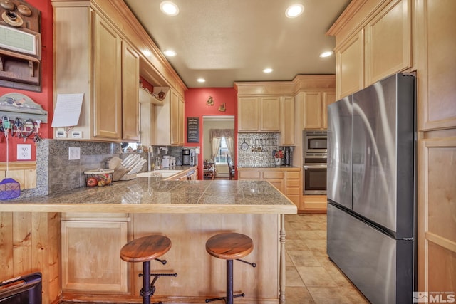 kitchen with a kitchen bar, kitchen peninsula, light brown cabinetry, and appliances with stainless steel finishes