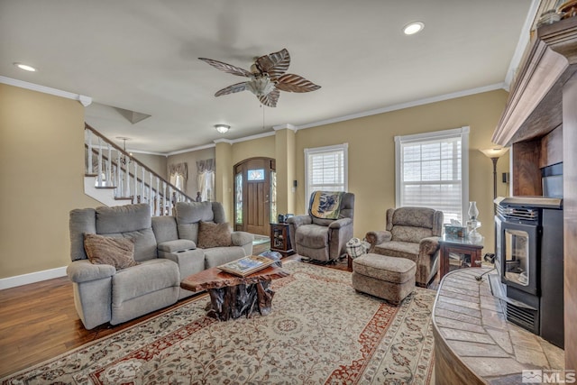 living room with a wood stove, ceiling fan, wood-type flooring, and ornamental molding