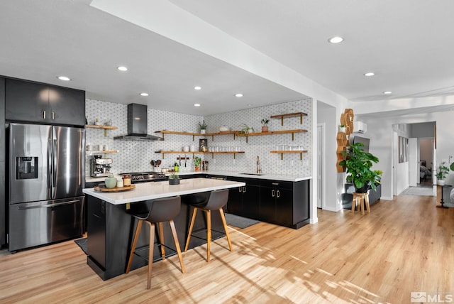 kitchen featuring decorative backsplash, stainless steel fridge with ice dispenser, a kitchen breakfast bar, and wall chimney range hood