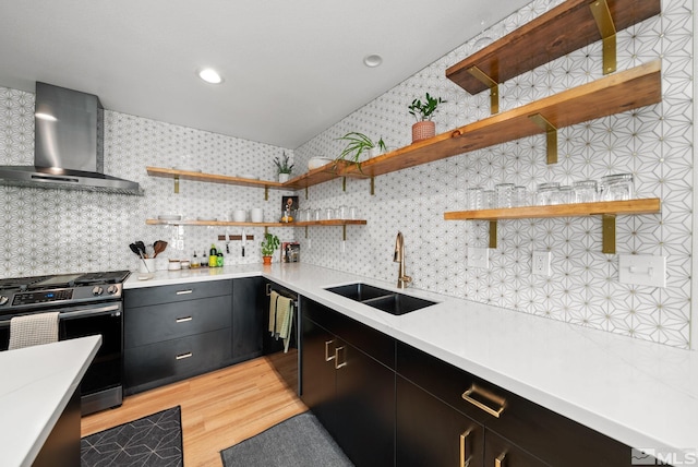 kitchen with light wood-type flooring, tasteful backsplash, wall chimney exhaust hood, stainless steel range, and sink