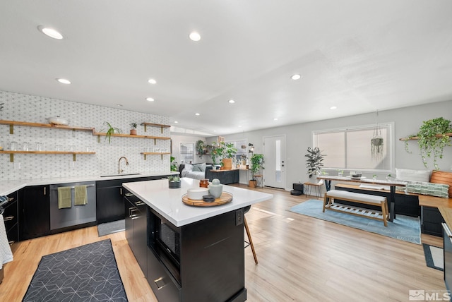 kitchen with sink, stainless steel dishwasher, light hardwood / wood-style floors, decorative backsplash, and a kitchen island