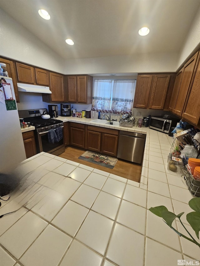 kitchen featuring stainless steel appliances, vaulted ceiling, sink, light tile patterned floors, and tile countertops