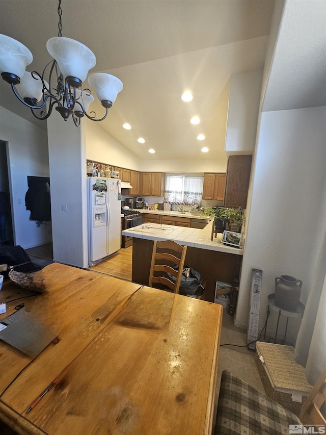 kitchen with lofted ceiling, tile counters, hanging light fixtures, white fridge with ice dispenser, and a notable chandelier