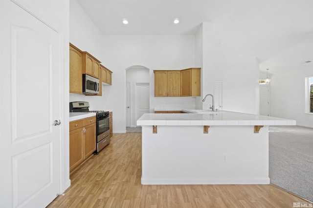 kitchen with tile countertops, sink, appliances with stainless steel finishes, light hardwood / wood-style floors, and a breakfast bar area