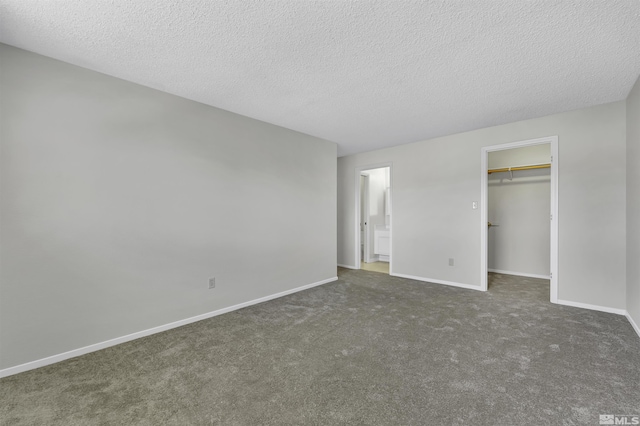 unfurnished bedroom with a textured ceiling, a walk in closet, dark carpet, and a closet