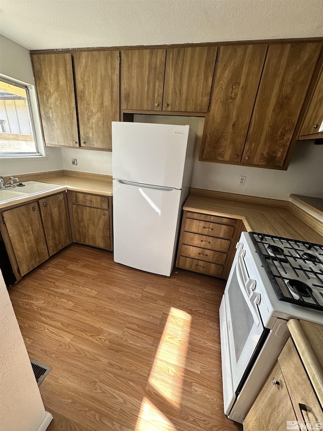 kitchen featuring a textured ceiling, sink, white appliances, and light hardwood / wood-style flooring