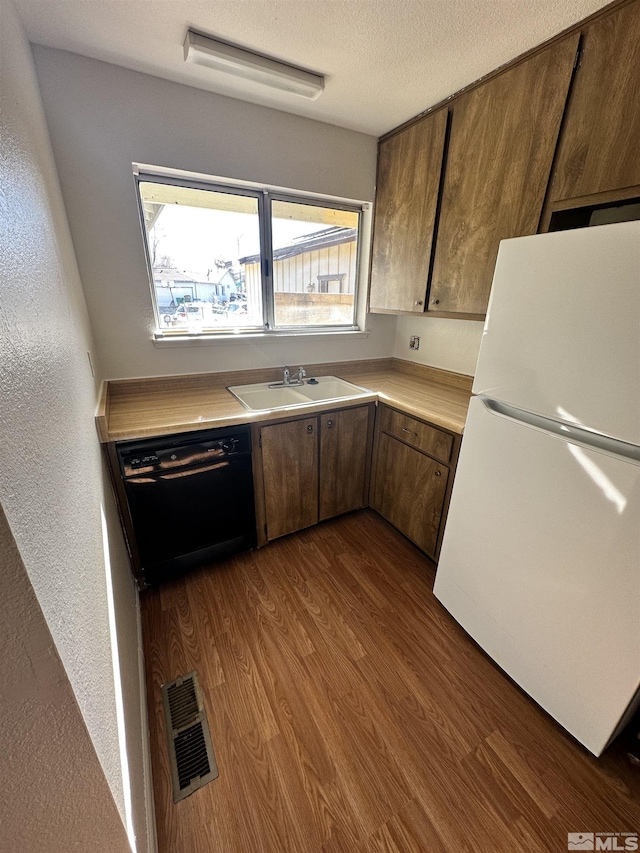 kitchen featuring hardwood / wood-style floors, white refrigerator, sink, black dishwasher, and a textured ceiling