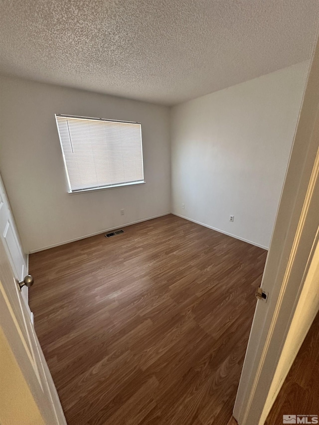 empty room featuring a textured ceiling and dark hardwood / wood-style floors