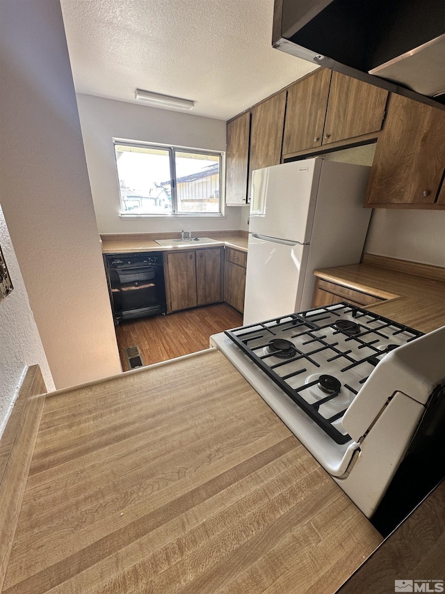 kitchen with dishwasher, light hardwood / wood-style flooring, white refrigerator, range with gas stovetop, and a textured ceiling