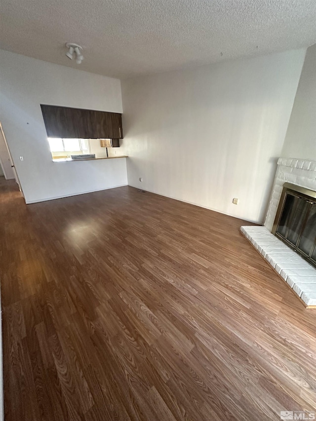 unfurnished living room with wood-type flooring, a textured ceiling, and a brick fireplace