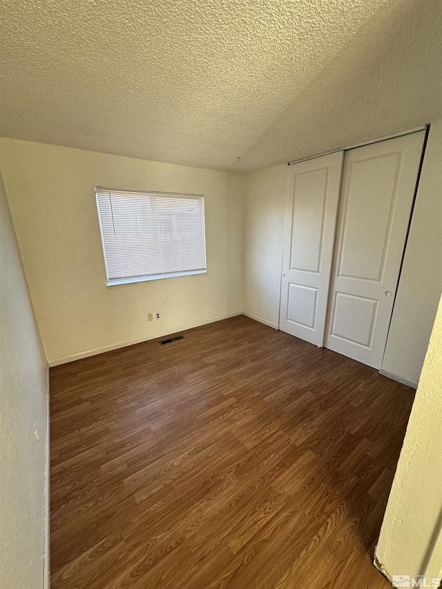 unfurnished bedroom featuring a textured ceiling, a closet, and dark wood-type flooring