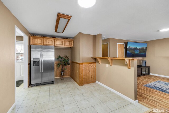 kitchen with kitchen peninsula, stainless steel fridge, a breakfast bar area, and wood walls