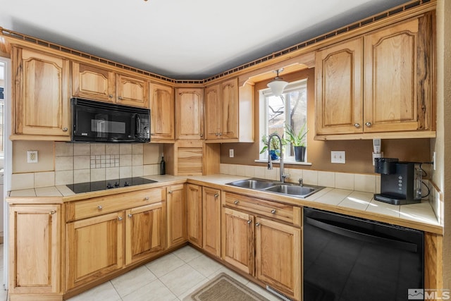 kitchen with backsplash, sink, black appliances, light tile patterned floors, and tile countertops