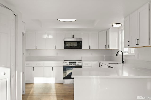 kitchen featuring white cabinets, kitchen peninsula, sink, and stainless steel range