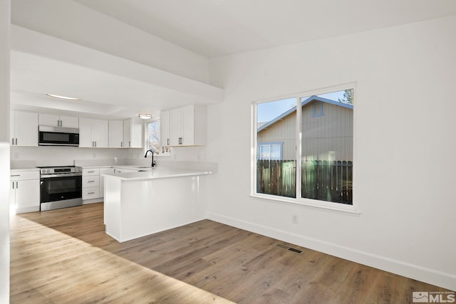 kitchen with sink, kitchen peninsula, light hardwood / wood-style flooring, appliances with stainless steel finishes, and white cabinetry