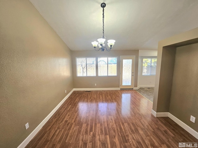 unfurnished dining area featuring dark hardwood / wood-style floors, lofted ceiling, and a chandelier