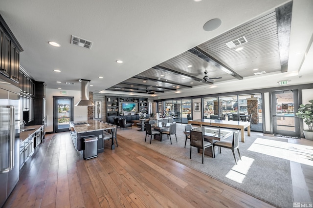 kitchen featuring ceiling fan, a center island, light stone countertops, wall chimney range hood, and dark hardwood / wood-style flooring