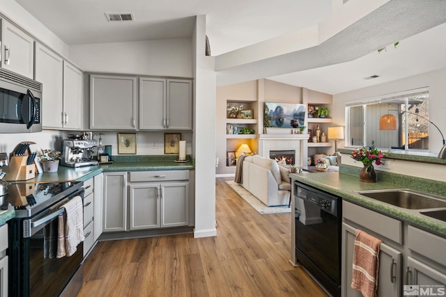 kitchen featuring appliances with stainless steel finishes, vaulted ceiling, sink, light hardwood / wood-style flooring, and gray cabinets