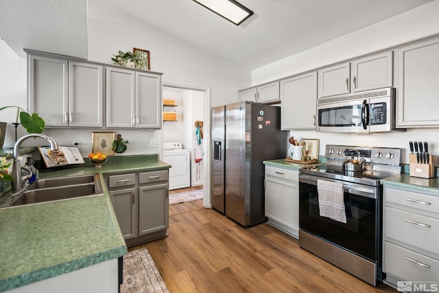 kitchen with lofted ceiling, sink, gray cabinets, washer / dryer, and stainless steel appliances