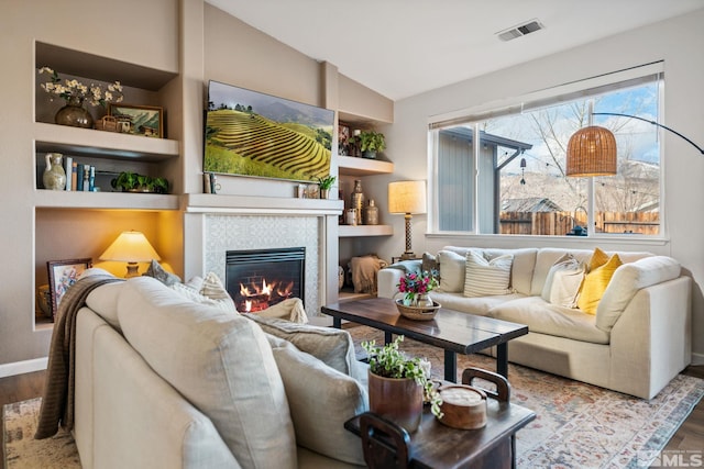 living room with lofted ceiling, a fireplace, built in features, and hardwood / wood-style flooring