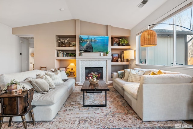 living room with a tile fireplace, vaulted ceiling, and built in features