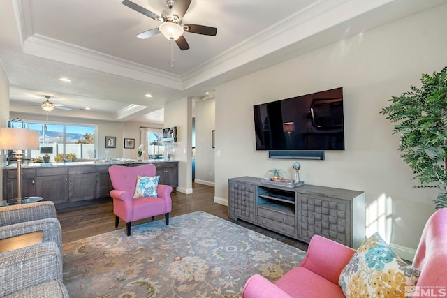 living room with a tray ceiling, ceiling fan, dark wood-type flooring, and ornamental molding