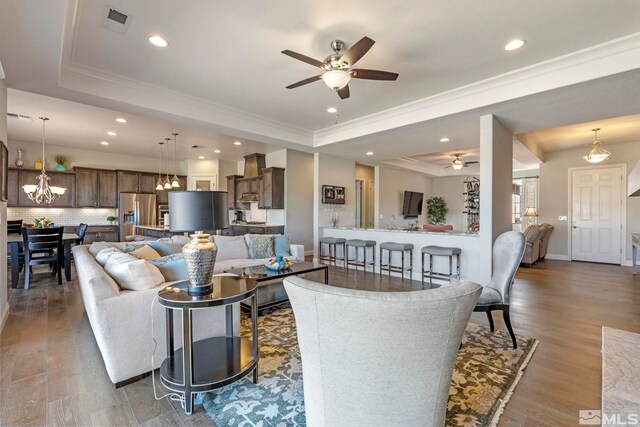 living room with wood-type flooring, ceiling fan with notable chandelier, a raised ceiling, and ornamental molding