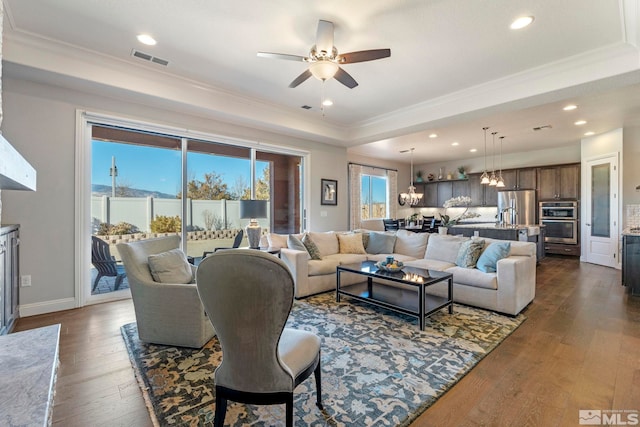 living room with ceiling fan with notable chandelier, dark hardwood / wood-style flooring, crown molding, and a tray ceiling