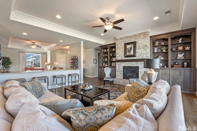 living room featuring ceiling fan, wood-type flooring, a fireplace, and a tray ceiling