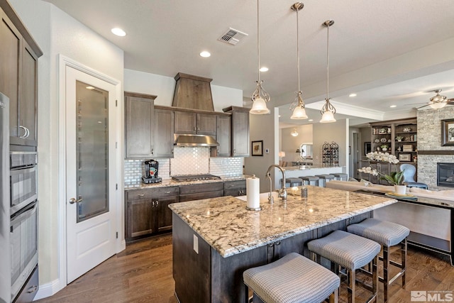 kitchen featuring light stone countertops, a center island with sink, hanging light fixtures, and appliances with stainless steel finishes