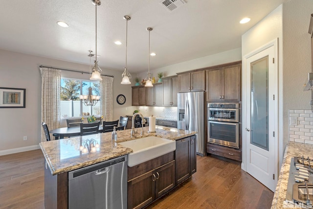 kitchen featuring light stone countertops, sink, tasteful backsplash, a kitchen island with sink, and appliances with stainless steel finishes