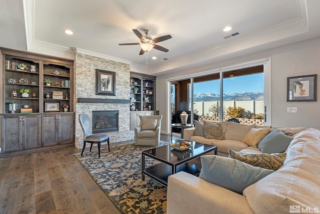 living room featuring built in shelves, ceiling fan, a mountain view, dark hardwood / wood-style floors, and a stone fireplace