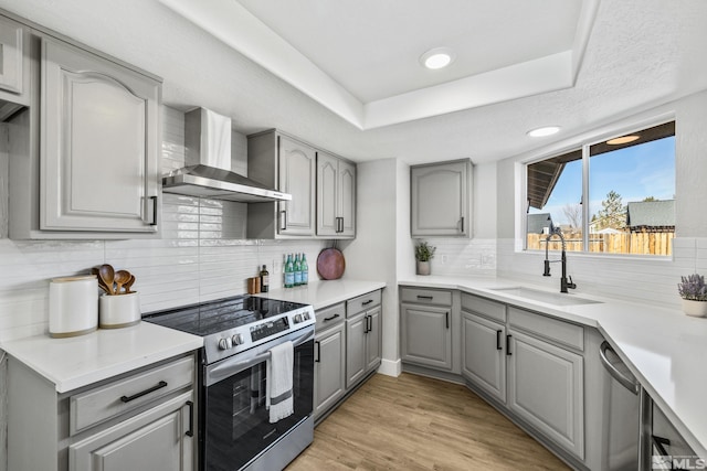 kitchen with gray cabinetry, stainless steel appliances, sink, wall chimney range hood, and light hardwood / wood-style flooring