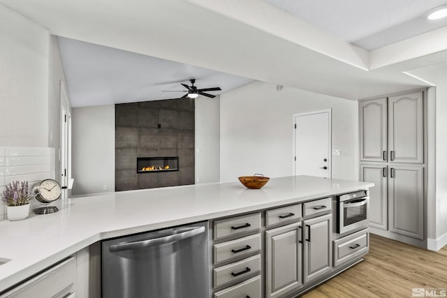 kitchen with gray cabinetry, ceiling fan, a tile fireplace, dishwasher, and light hardwood / wood-style floors