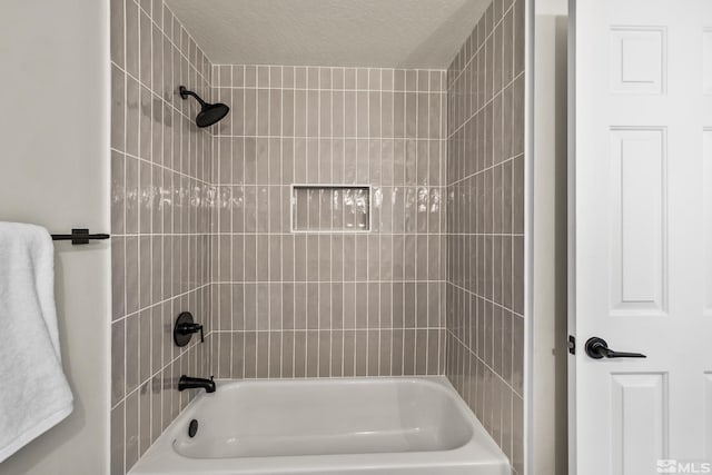 bathroom featuring a textured ceiling and tiled shower / bath