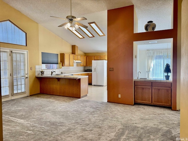 kitchen featuring kitchen peninsula, backsplash, light colored carpet, white refrigerator with ice dispenser, and tile counters