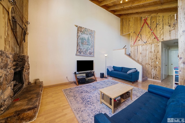 living room featuring wooden walls, light hardwood / wood-style flooring, a fireplace, beamed ceiling, and wood ceiling