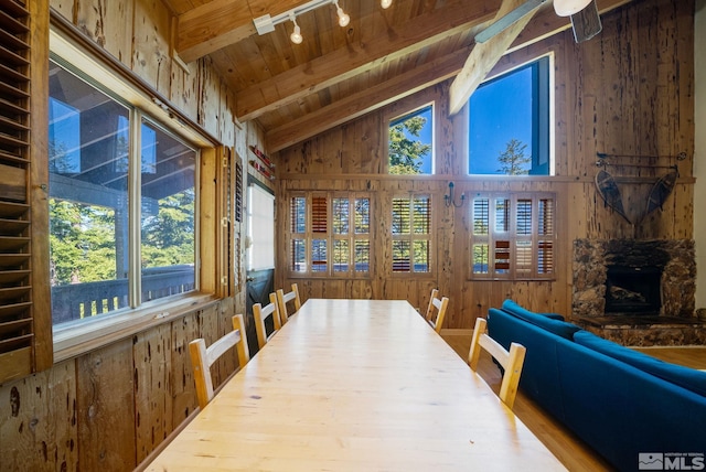 dining room featuring ceiling fan, vaulted ceiling with beams, track lighting, a fireplace, and wood ceiling