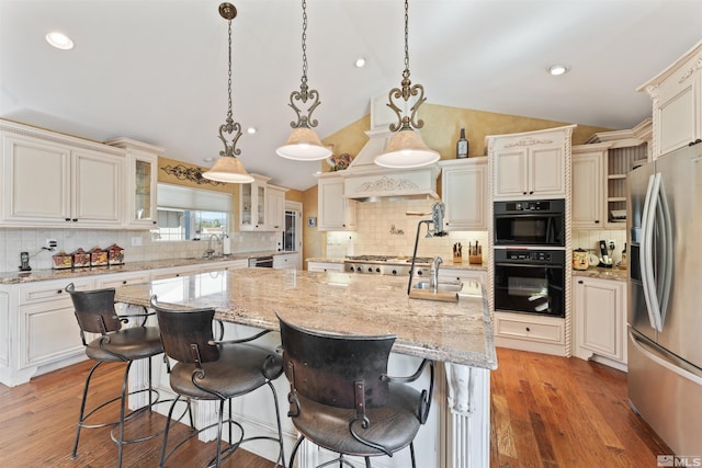 kitchen with hanging light fixtures, stainless steel appliances, lofted ceiling, a kitchen island with sink, and a breakfast bar