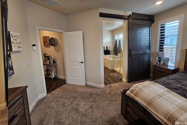 bedroom featuring ensuite bathroom, dark carpet, multiple windows, and a barn door