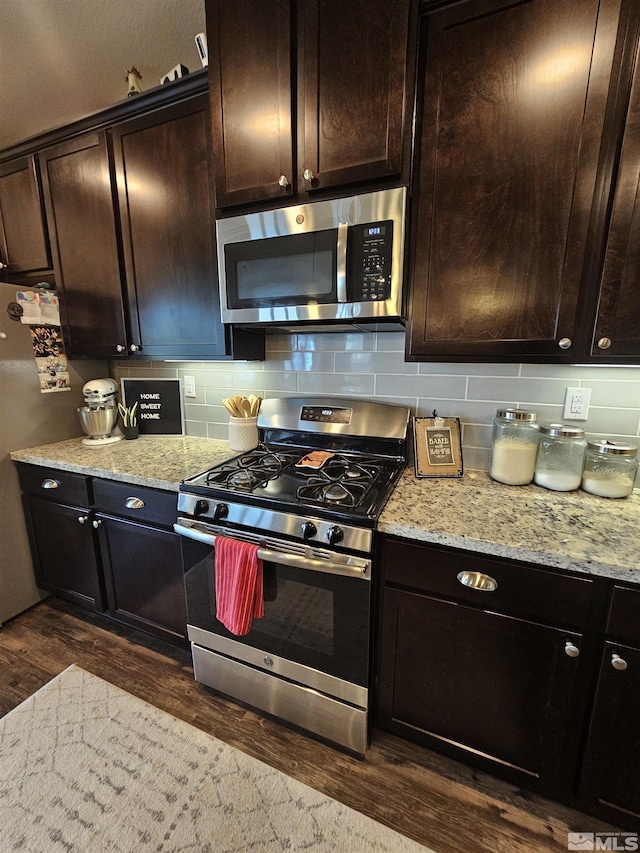 kitchen with stainless steel appliances, light stone countertops, dark hardwood / wood-style floors, dark brown cabinets, and tasteful backsplash