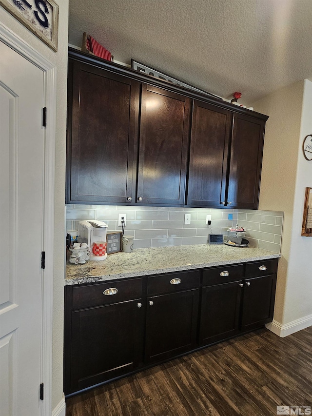 kitchen featuring a textured ceiling, light stone counters, tasteful backsplash, dark brown cabinetry, and dark hardwood / wood-style flooring