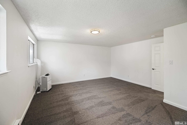 spare room with a textured ceiling and dark colored carpet