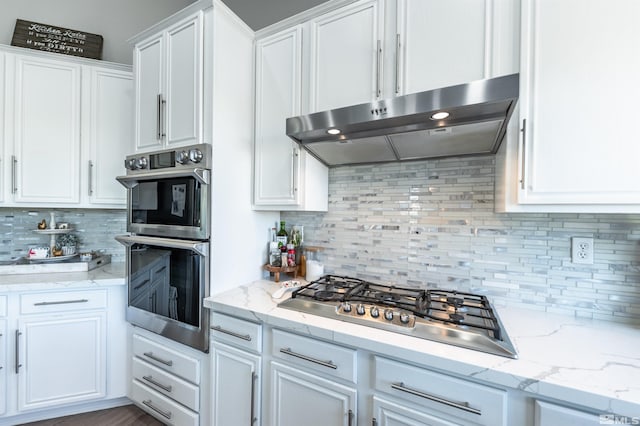 kitchen featuring tasteful backsplash, light stone countertops, white cabinets, and appliances with stainless steel finishes