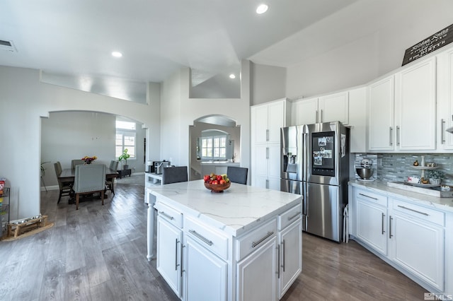 kitchen with light stone countertops, stainless steel refrigerator with ice dispenser, dark hardwood / wood-style flooring, a kitchen island, and white cabinetry