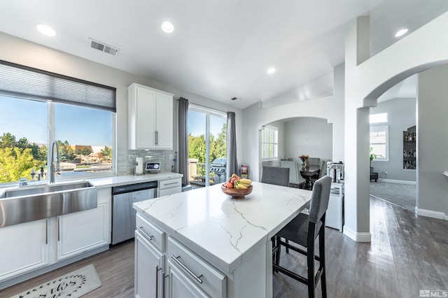 kitchen with sink, stainless steel dishwasher, light stone countertops, a kitchen island, and white cabinetry